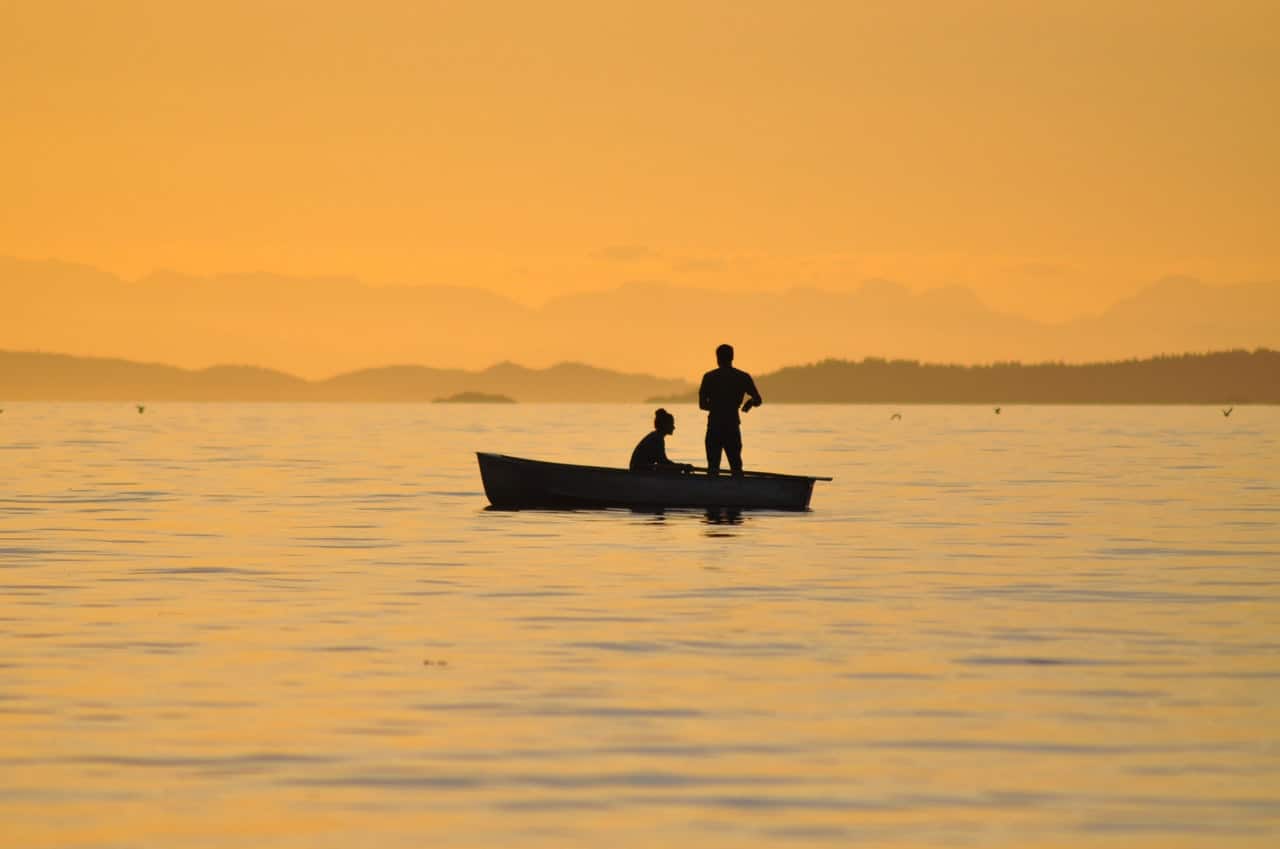 two men fishing in a boat at sunset