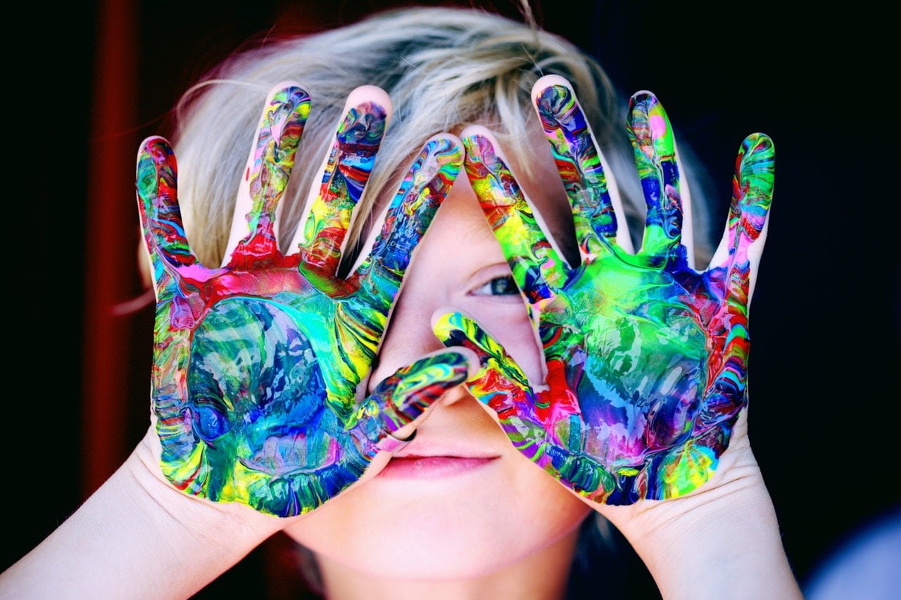 little boy holding his hands with paint on them in front on his face