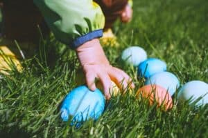 small childs hand reaching into grass to collect colourful easter eggs - easter egg hunt