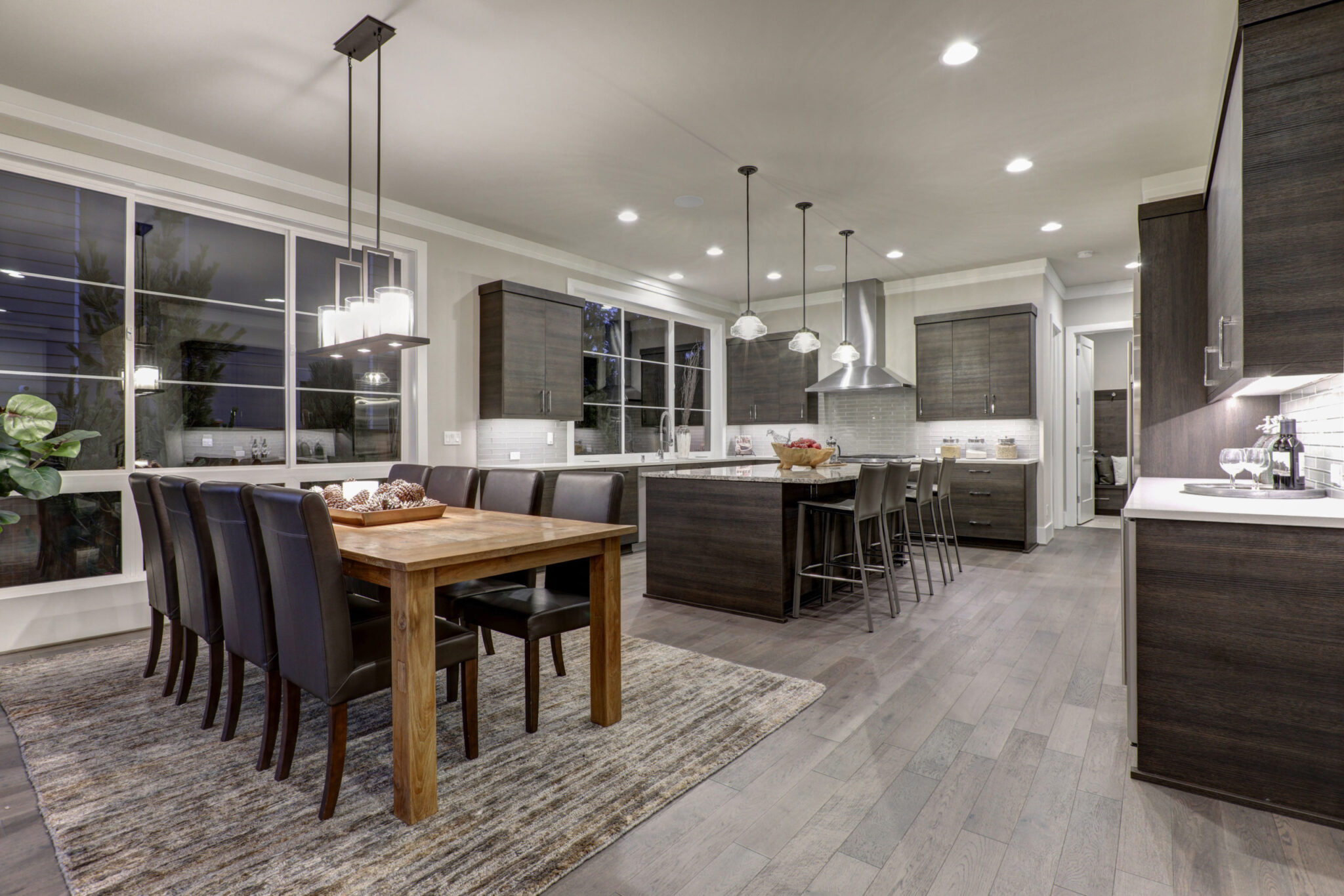 Luxury New construction home with open floor plan: dining and kitchen design. Rustic wood dining table matches with modern style leather chairs. Kitchen accented with dark cabinetry. Northwest USA
