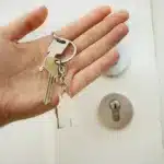 person holding keys in hand in front of a door with a house keychain