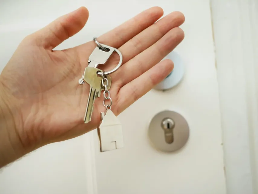 person holding keys in hand in front of a door with a house keychain
