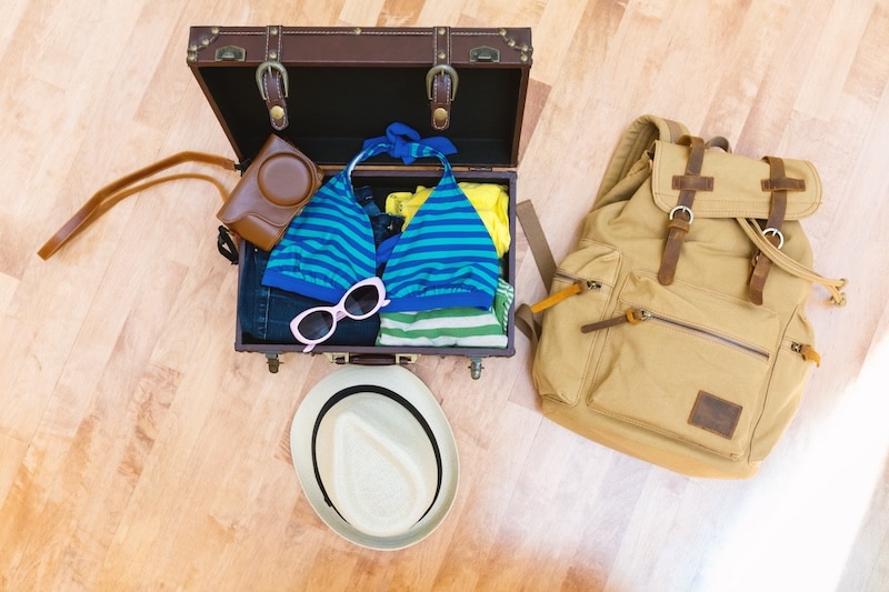 Open suitcase with summer clothes packed and folded, sunglasses, hat, bathingsuit and camera