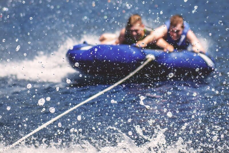 two men tubing behind a boat with splashing water - summer activities