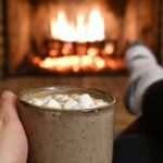 person hitting by a fire with a cup of hot chocolate