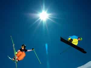 two skiers making a jump - photo taken from the ground - bright blue sky and sun shining 