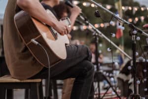 person playing a guitar on an outdoor stage - view of the guitar, legs and arms - indie music - outdoor festival