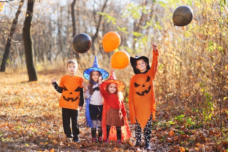 a group of children in carnival costumes with orange and black balloons and a Jack pumpkin in their hands celebrate Halloween.