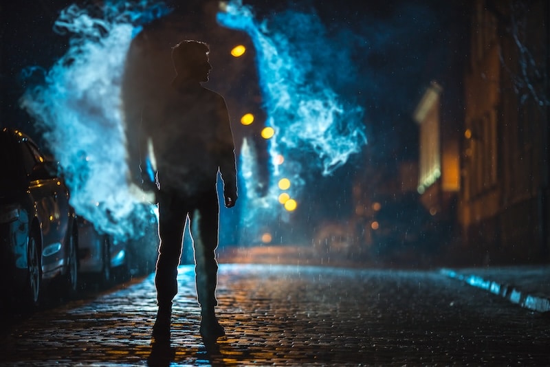 The man stand near the cloud of smoke. Evening night time