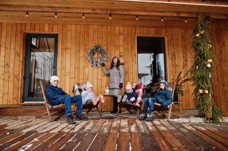 Attractive mother with her four kids on the terrace of a wooden house in winter day.