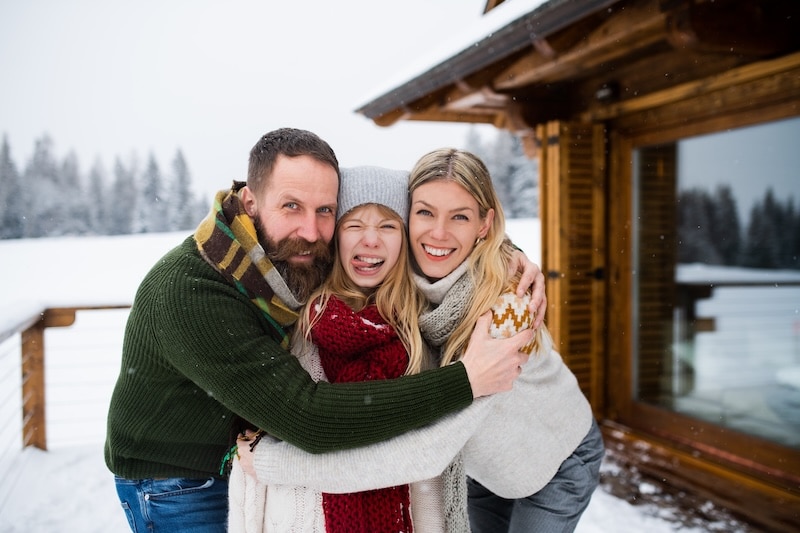 Portrait of a family with small daughter outdoors in winter holiday cottage, looking at camera.
