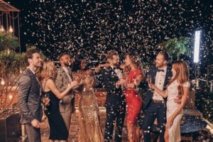 Group of happy people in formalwear having fun together with confetti flying all around