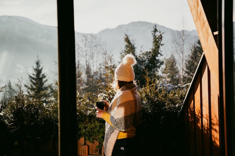 woman enjoying hot cup of tea on terrace in winter mountains ski holiday lodging