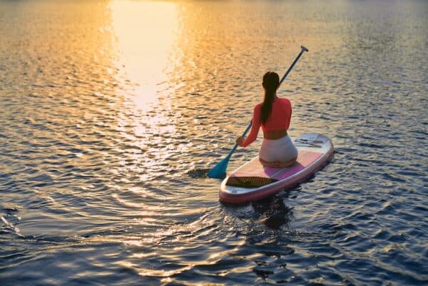 Young female athlete spending evening time on city lake for practising in sup boarding. Beautiful sunset on background. Reflection on water.