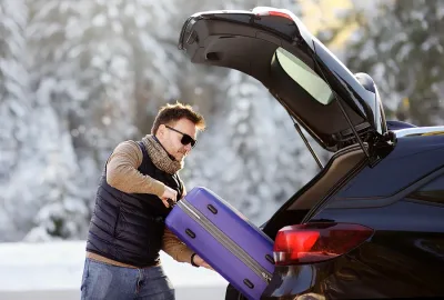 Handsome man going to vacations, loading his suitcase in car trunk. Winter automobile trip in the countryside. Vacation in mountains. Alps, Bavaria, Germany (Deutschland)