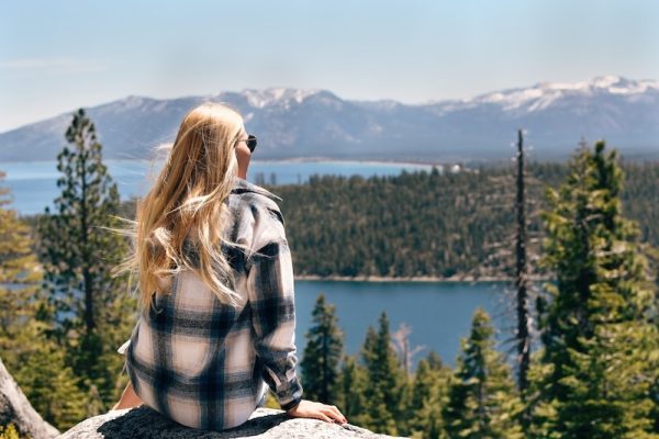 blonde woman sitting on a rock at a viewpoint in north lake tahoe overlooking the lake and distant mountains in the summer on a sunny day
